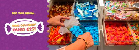Assorted sweets selection showcasing blue sweets being placed into a paper bag and cola bottle sweets, pencil sweets, fizzy sweets and foam sweets in the background with a banner reading 'Free Delivery Over £25'